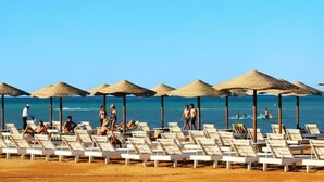 Una platja amb gandules i sombrerets de palla, cel serè i un vela al lluny.