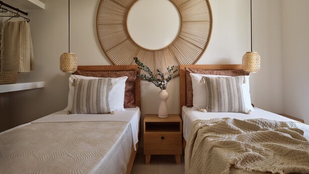 Une chambre avec deux lits, un grand miroir rond et des lampes en osier.