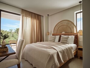 Ein Schlafzimmer mit einem großen Bett, einem Korbschlafbrett, einem Holznachttisch, einem Korbstuhl und Blick auf Grünfläche.
