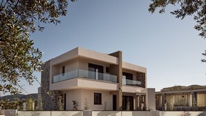 Une maison moderne à deux étages, dotée d’un balcon, d’une façade en pierre et offrant une vue sur le paysage environnant.
