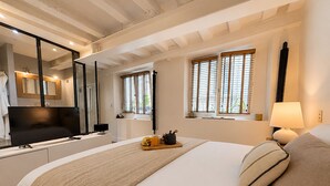 A bedroom with a bed, a TV, a bedside table, a lamp, and a window with blinds. - L'appartement Charlot C (Paris)