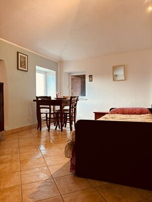 Una stanza con un letto, un tavolo da pranzo con sedie, una piccola finestra e una porta che dà su un'altra stanza.