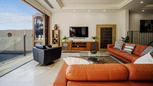 Een moderne woonkamer met een grote televisie, leren banken en een glazen deur naar een balkon.