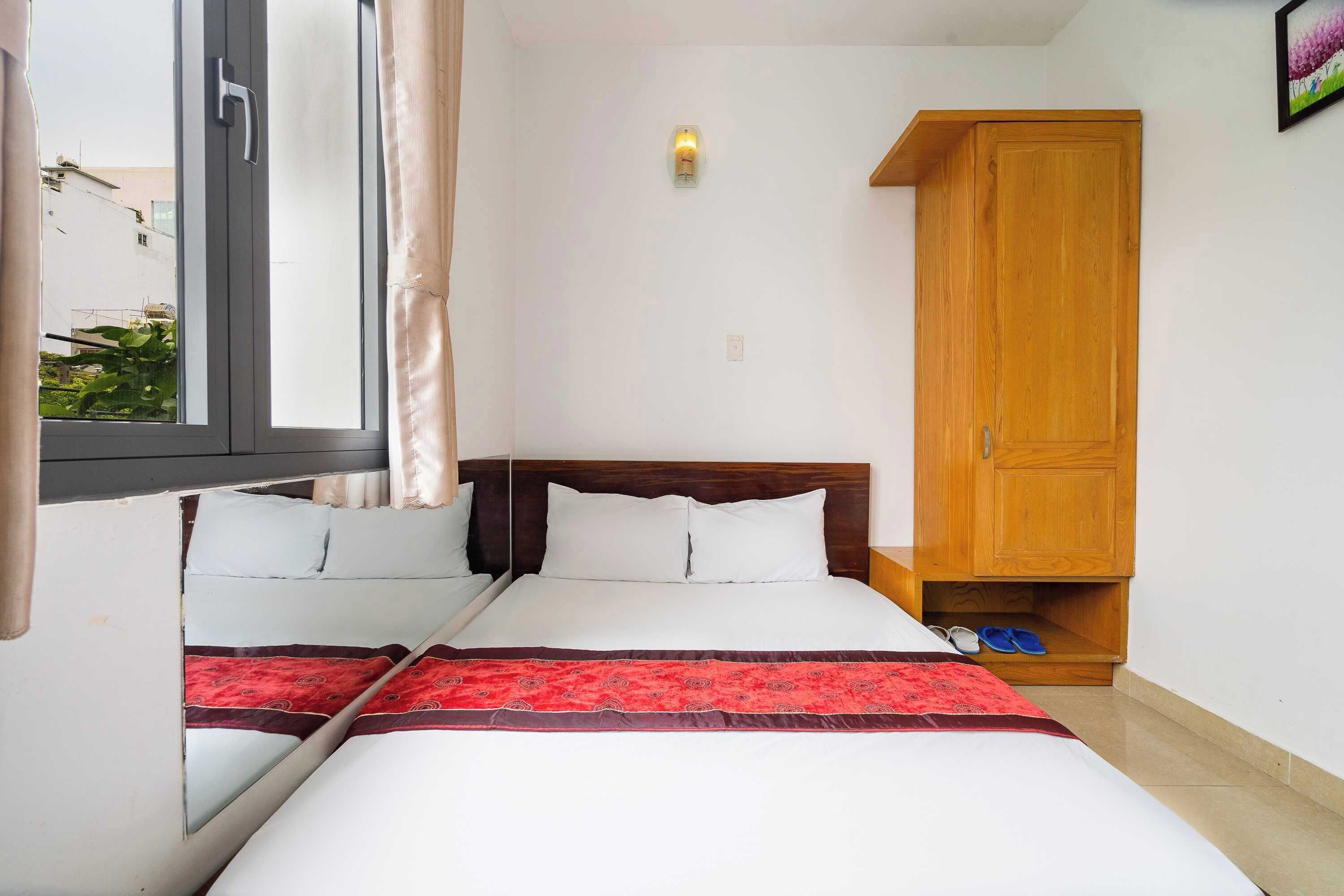 A bedroom with a bed, a wardrobe, a window, and a wall-mounted light fixture.