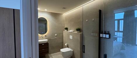A modern bathroom with a glass shower enclosure, a round mirror, and a wooden vanity.