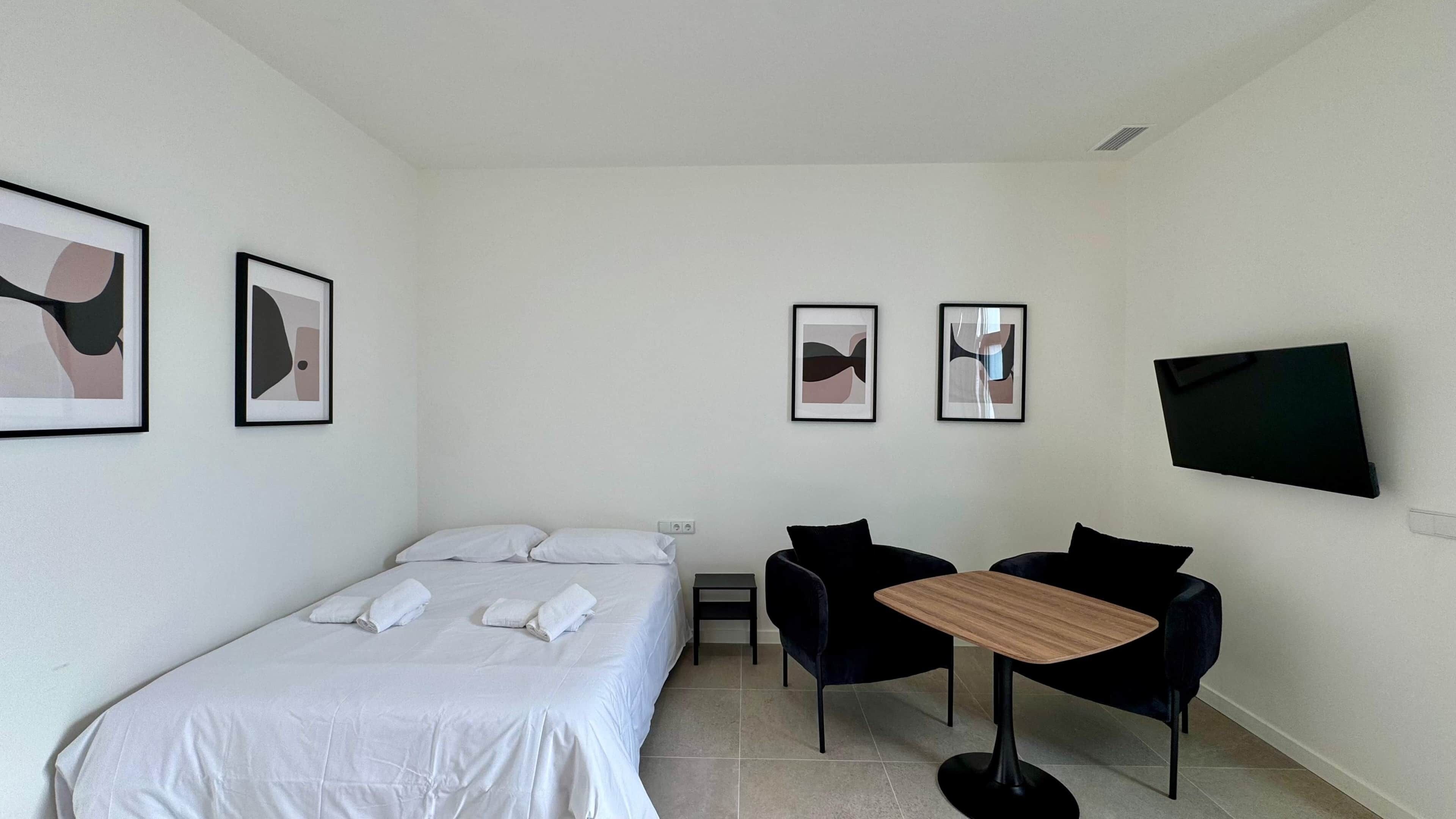 Une chambre d’hôtel avec un lit, deux chaises, une petite table et un téléviseur fixé au mur.