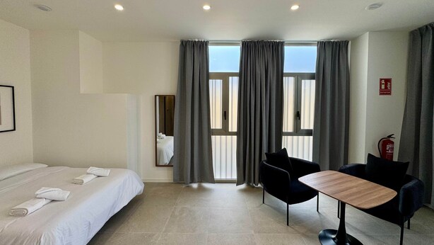 Habitación de hotel con cama, una mesa, dos sillas, un espejo y una ventana con cortinas.