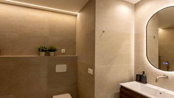 Un baño moderno con inodoro blanco, tocador de madera, espejo grande y estante de pared con plantas.