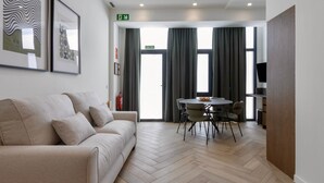 Una sala de estar moderna con un sofá color beige, una mesa de comedor con sillas y un amplio ventanal con cortinas.