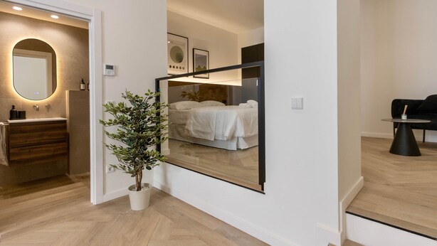 Habitación de hotel moderna con un espejo grande que refleja la cama y una planta en maceta.