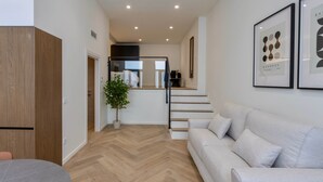 A modern living room with a sofa, a dining table, and a staircase leading to an upper level. - One Tower Loft 08 (Valencia)