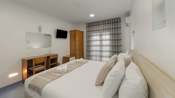 Ein Hotelzimmer mit einem großen Bett, einem Holztisch, einem Fernseher und einem Fenster mit Vorhängen.