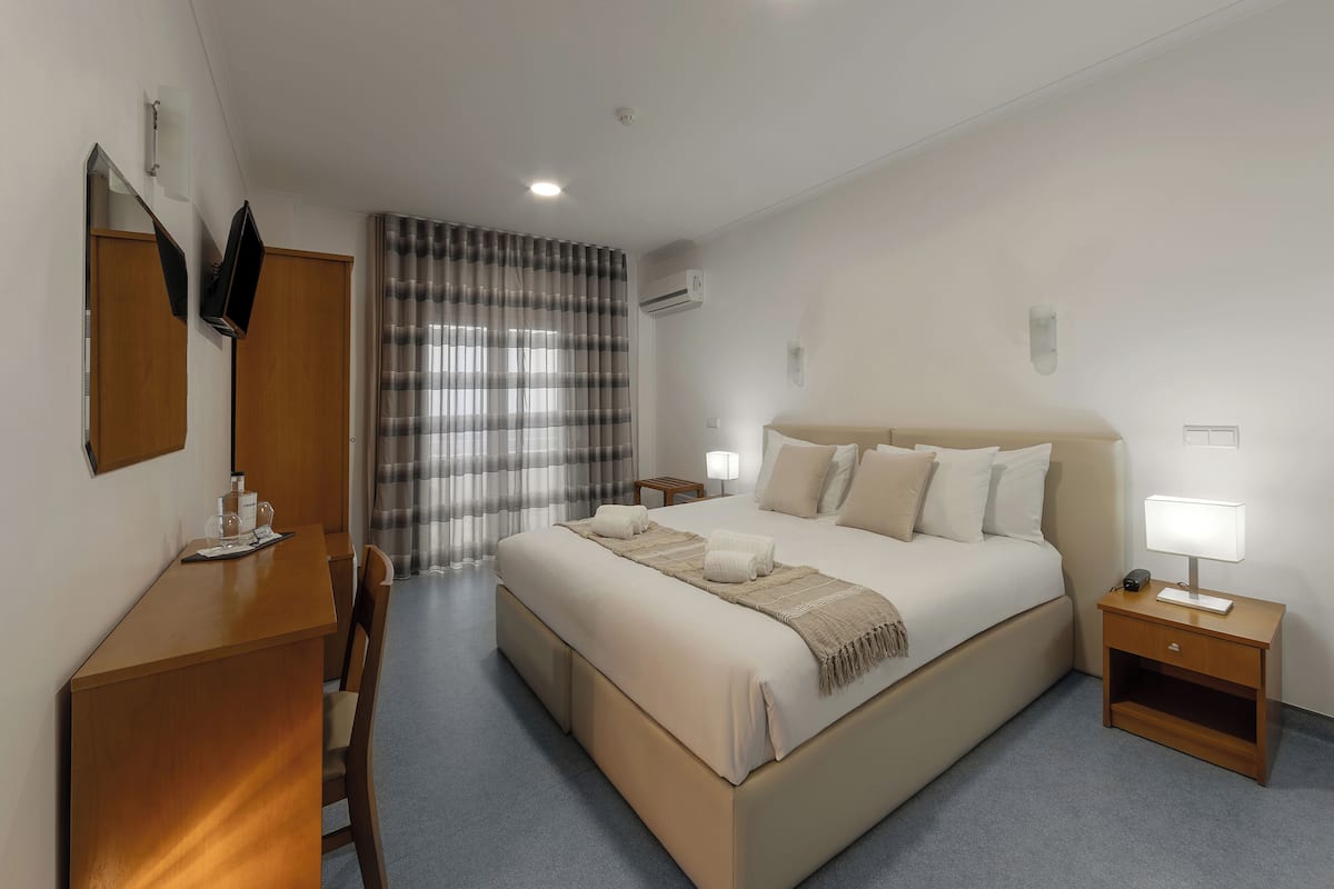 Hotellihuone, jossa on suuri sänky, työpöytä, tuoli, yöpöytä lampun kanssa ja ikkuna, jossa on verhot.