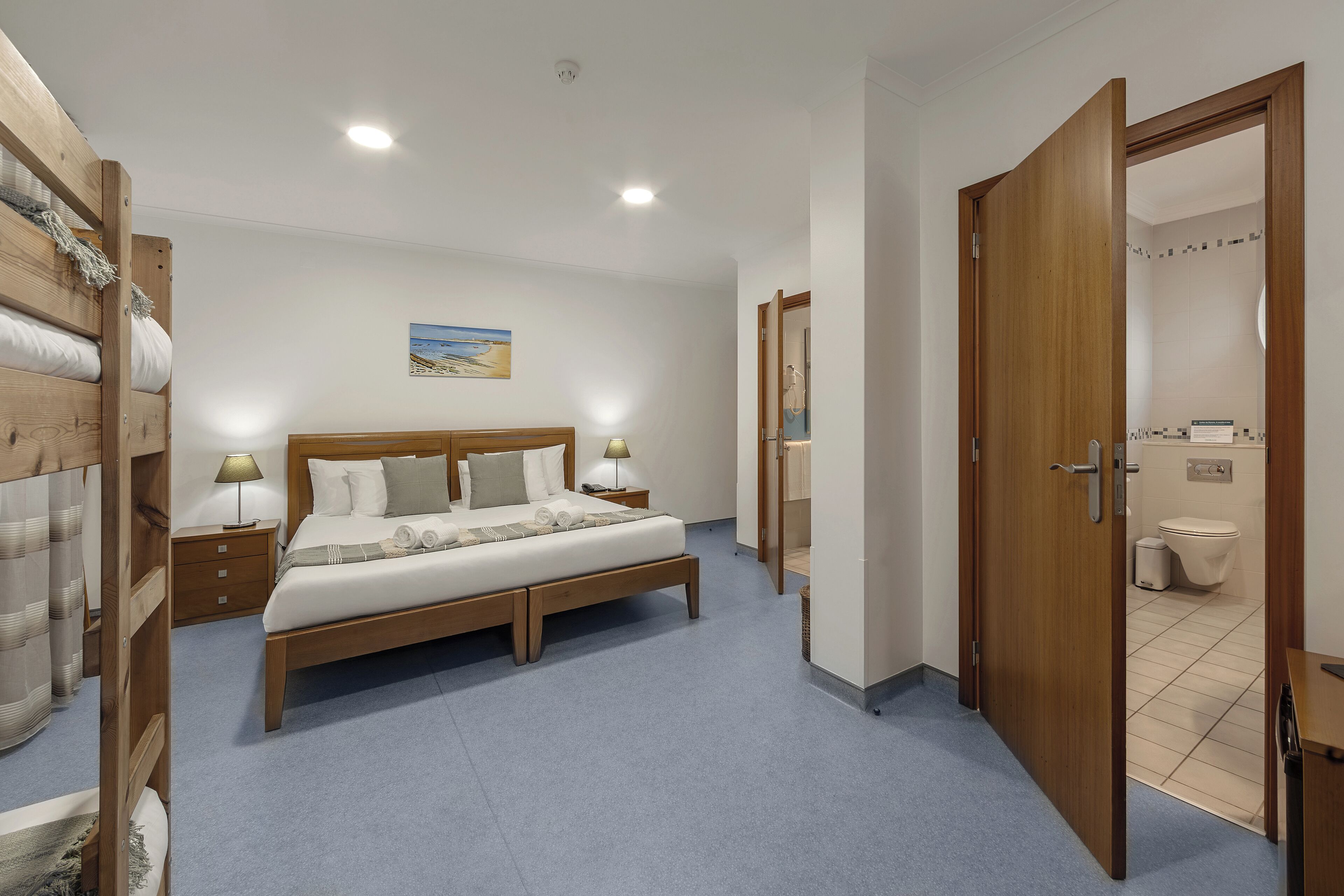 Un dormitorio con cama de madera, mesitas de noche y un baño visible a través de una puerta abierta.