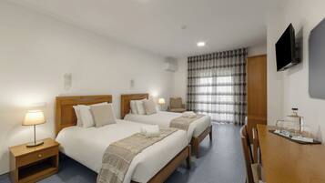 Habitación de hotel con dos camas, un escritorio, una silla, un televisor y una ventana con cortinas.