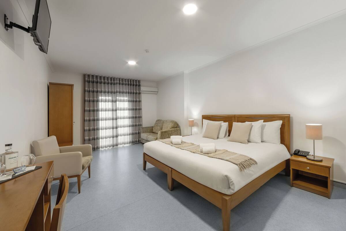 Hotellihuone, jossa on suuri sänky, työpöytä, tuoli, televisio ja ikkuna, jossa on verhot.