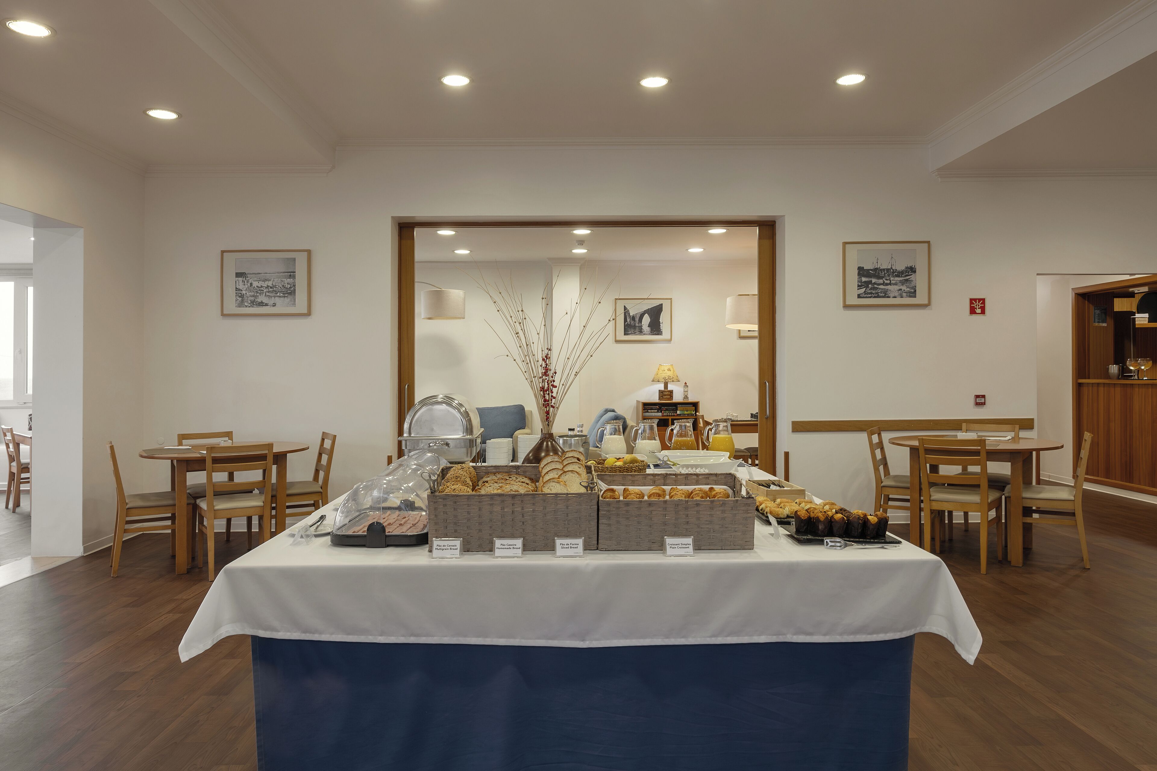 Een ontbijtbuffet met diverse gerechten en een koffiehoek, omringd door houten stoelen en tafels.