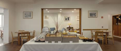 Een ontbijtbuffet met diverse gerechten en een koffiehoek, omringd door houten stoelen en tafels.