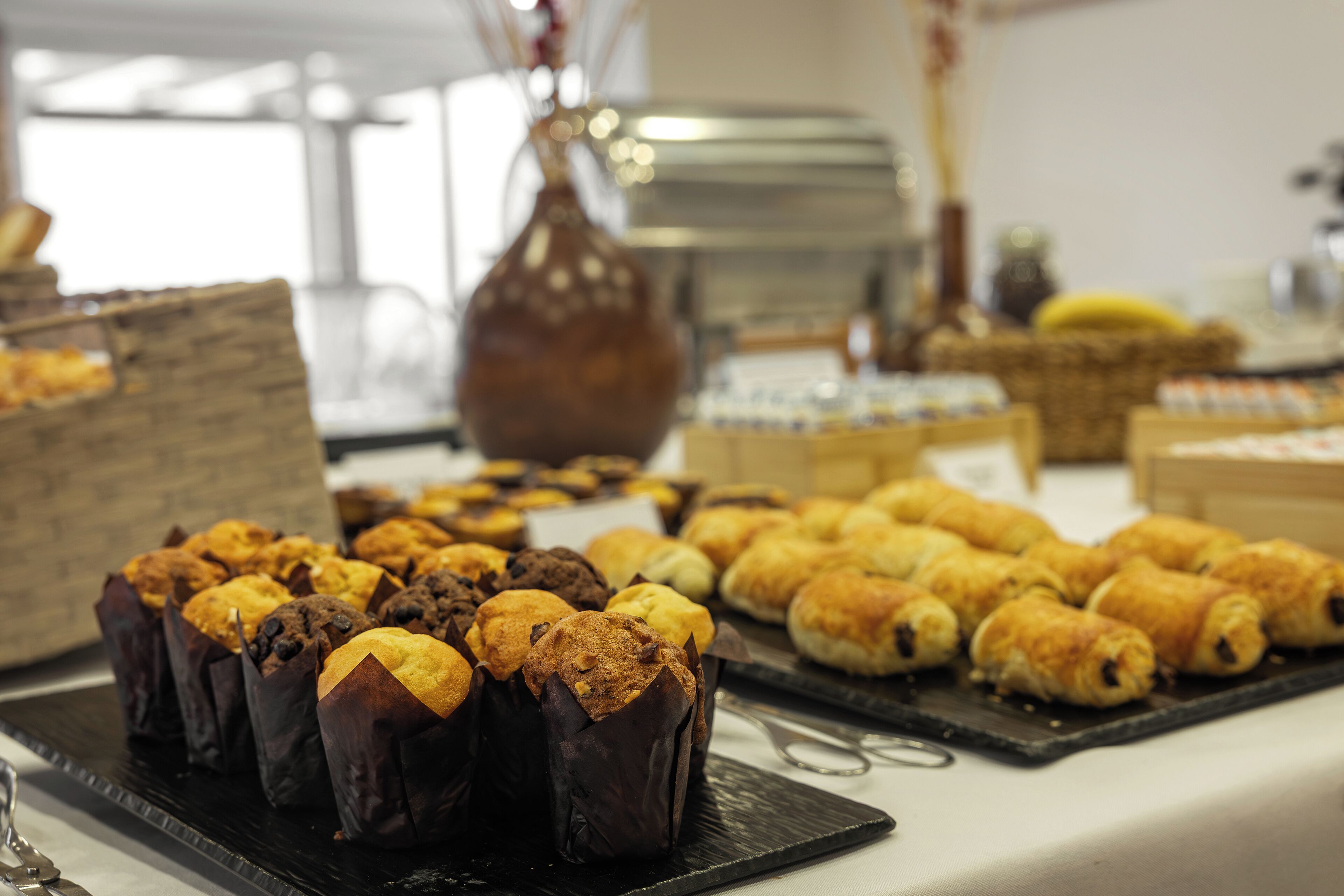 A buffet table with various baked goods, including muffins and pastries.