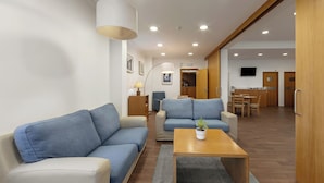 Ein modernes Wohnzimmer mit einer Couch, einem Couchtisch und einer Lampe. Ein Fernseher ist an der Wand befestigt und es gibt ein Holzregal.