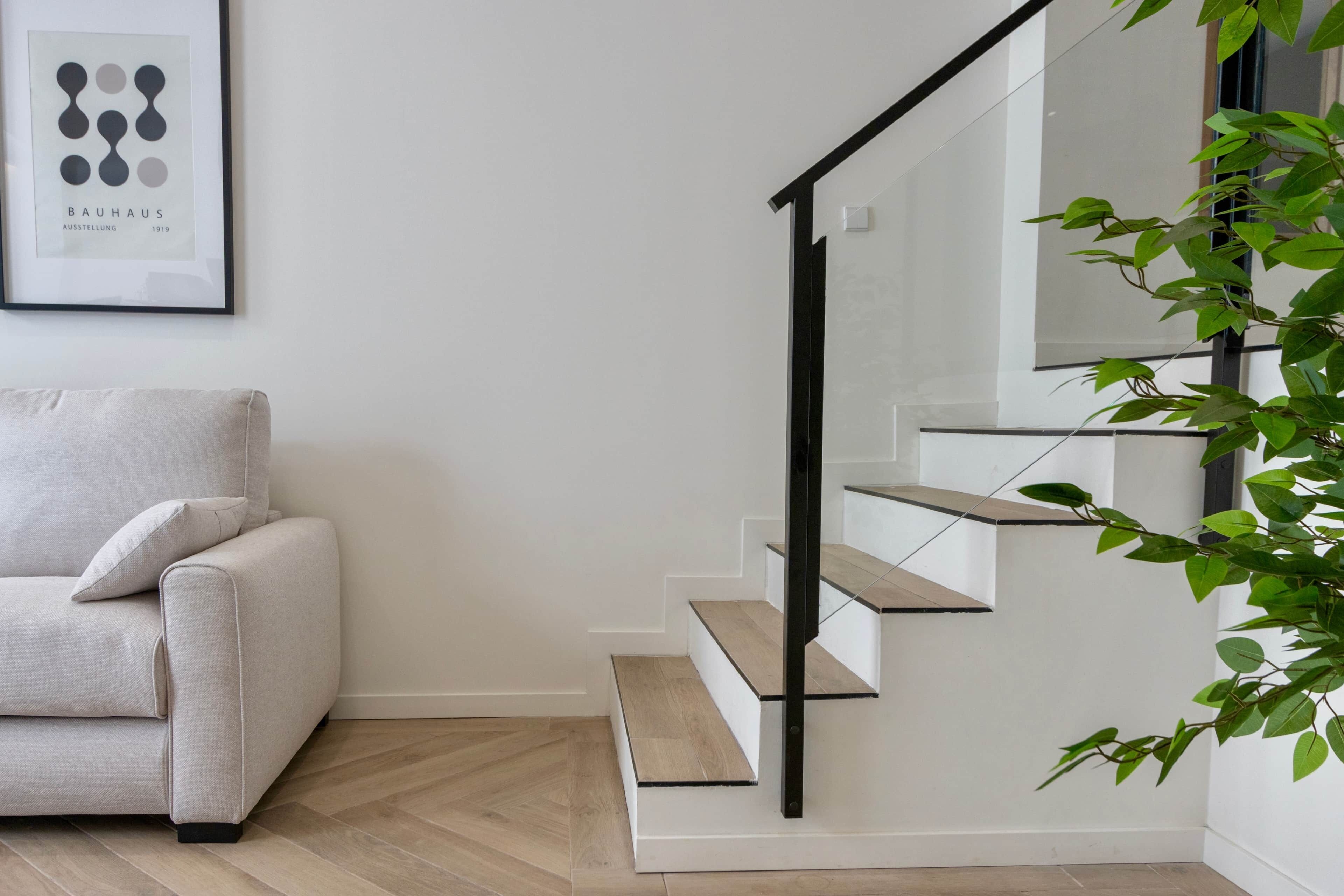 A staircase with a glass railing, a light-colored sofa, and a framed picture on the wall.
