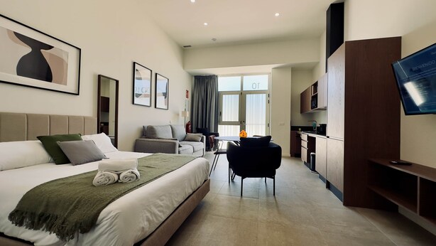 A hotel room with a bed, a desk, a chair, a television, and a kitchen area. - Plaza Tower Loft 10 (Valencia)