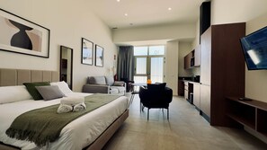 Una habitación de hotel con cama, escritorio, silla, televisión y una zona de cocina.