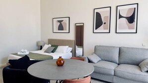 A hotel room with a bed, a grey sofa, a round table with a vase, and abstract wall art. - Plaza Tower Loft 10 (Valencia)