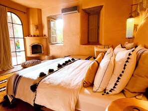 Ein Schlafzimmer mit Kamin, einem Bett mit weißer Bettwäsche und Zierkissen, einem Fenster mit Vorhängen und einer Hängelampe.
