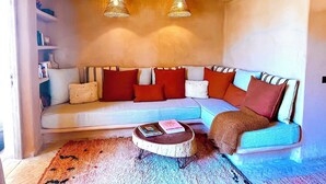 Uma sala de estar aconchegante com um sofá seccional, duas luminárias pendentes, uma mesa de centro e uma estante.