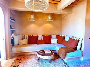 Ein gemütliches Wohnzimmer mit einer Eckcouch, zwei Pendelleuchten, einem Couchtisch und einem Bücherregal.