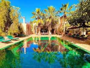 A swimming pool with lounge chairs and palm trees. - Palais Bouchka (Essaouira)