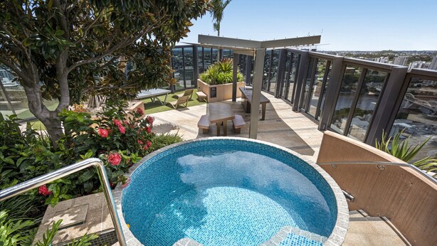 A rooftop pool with a glass balustrade, surrounded by greenery and a seating area. - Stylish 1-bed Apartment in South Brisbane (Brisbane)