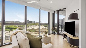 A modern living room with a large window, a ceiling fan, a flat-screen TV, and a round coffee table. - Stylish 1-bed Apartment in South Brisbane (Brisbane)