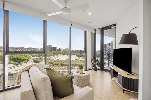A modern living room with a large window, a ceiling fan, a flat-screen TV, and a round coffee table. - Stylish 1-bed Apartment in South Brisbane (Brisbane)