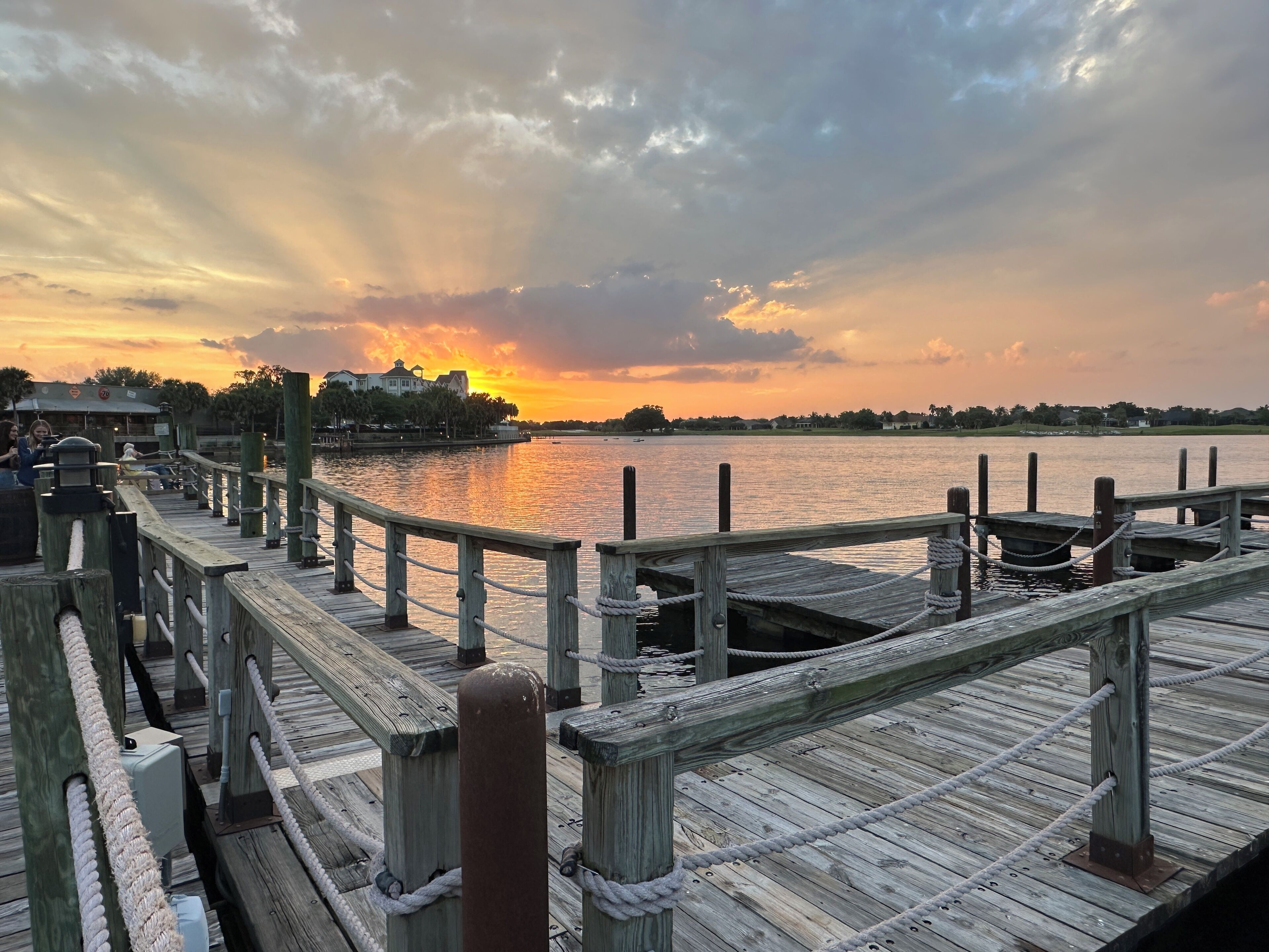 A wooden pier with a rope barrier, leading to a dock with moored boats.