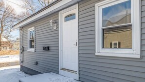 A single-story house with a white door and windows, a small porch, and a snow-covered ground. - Peaceful Bangor Getaway | Clean & Cozy 2BR Home (Bangor)