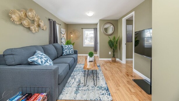 A living room with a grey sofa, a coffee table, and a TV. There is a window with curtains, a mirror, and wall art. - Peaceful Bangor Getaway | Clean & Cozy 2BR Home (Bangor)