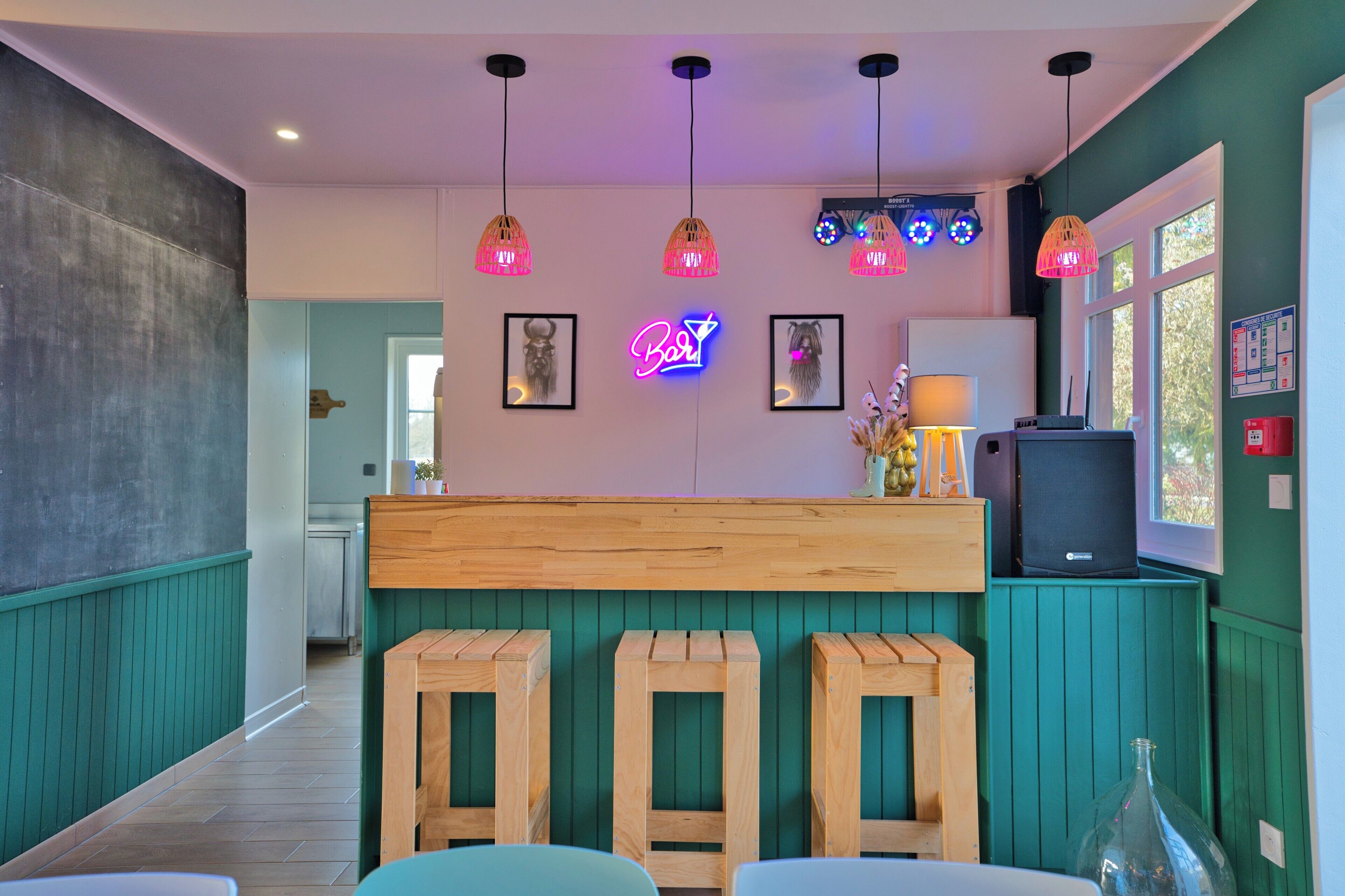 A restaurant interior with wooden bar stools, pendant lights, framed pictures, and a neon sign.