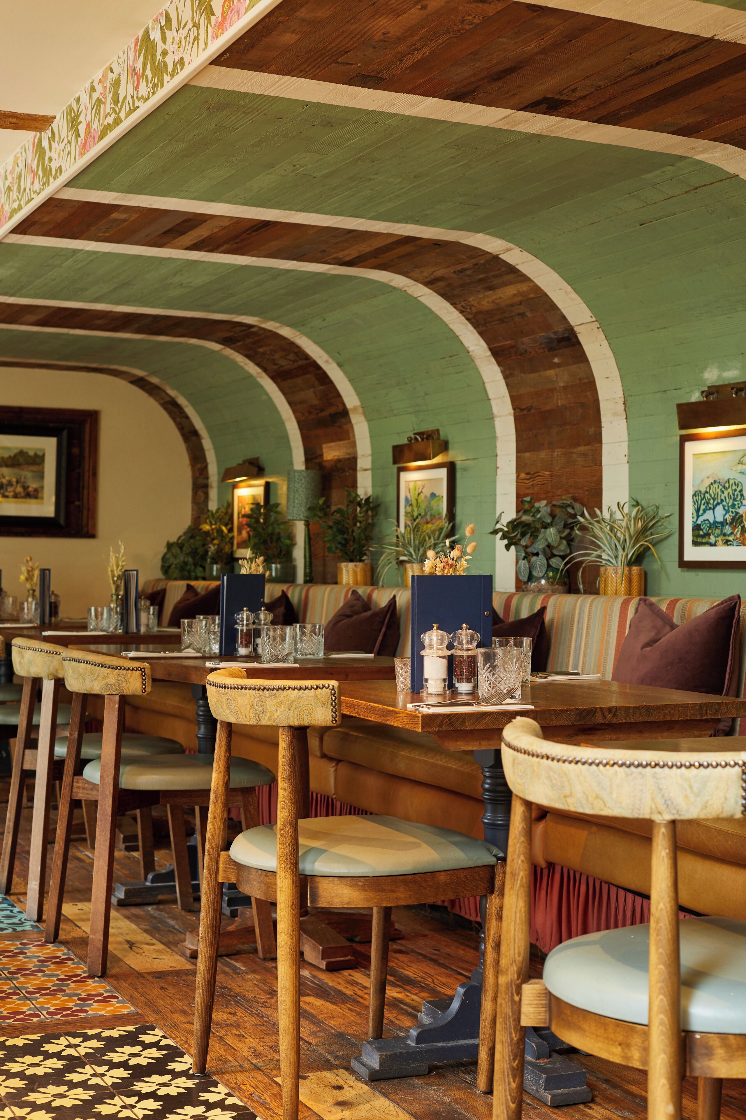 A restaurant interior with wooden tables and chairs, green walls, and arched ceilings.