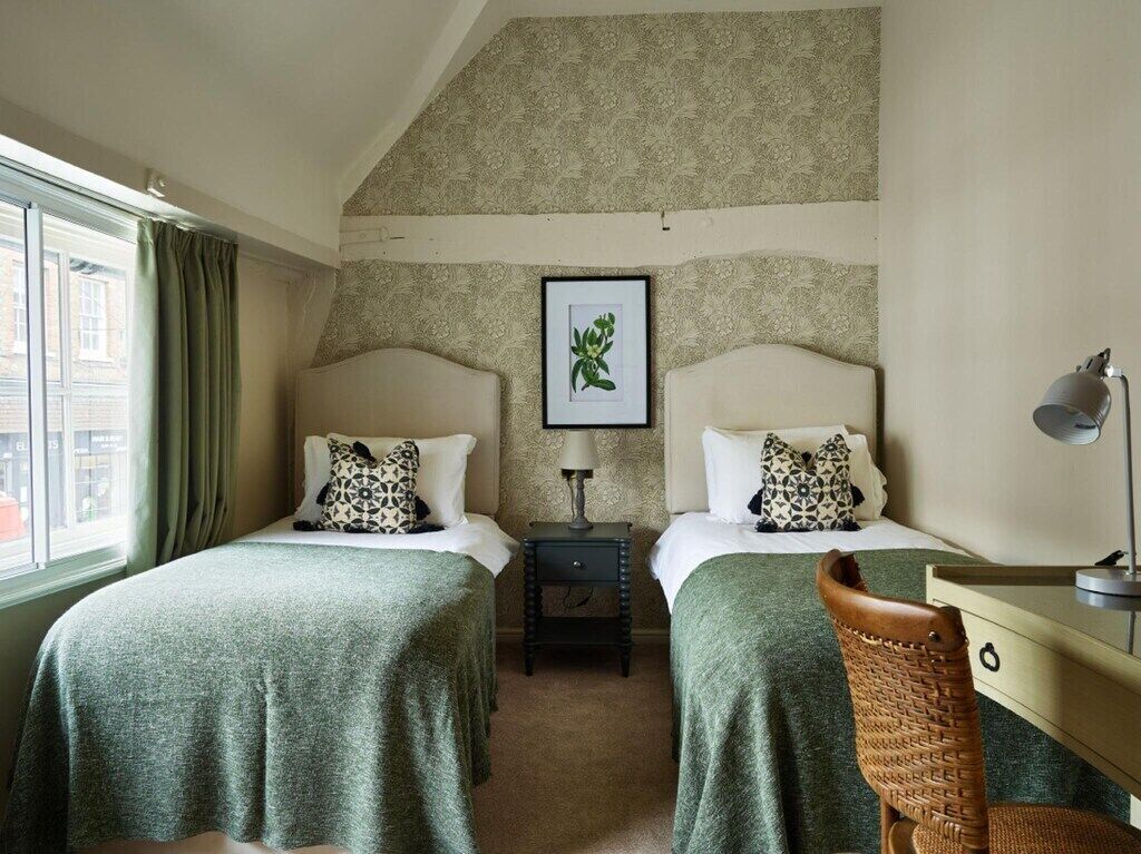 A room with two beds, a desk, a lamp, and a framed picture on the wall.