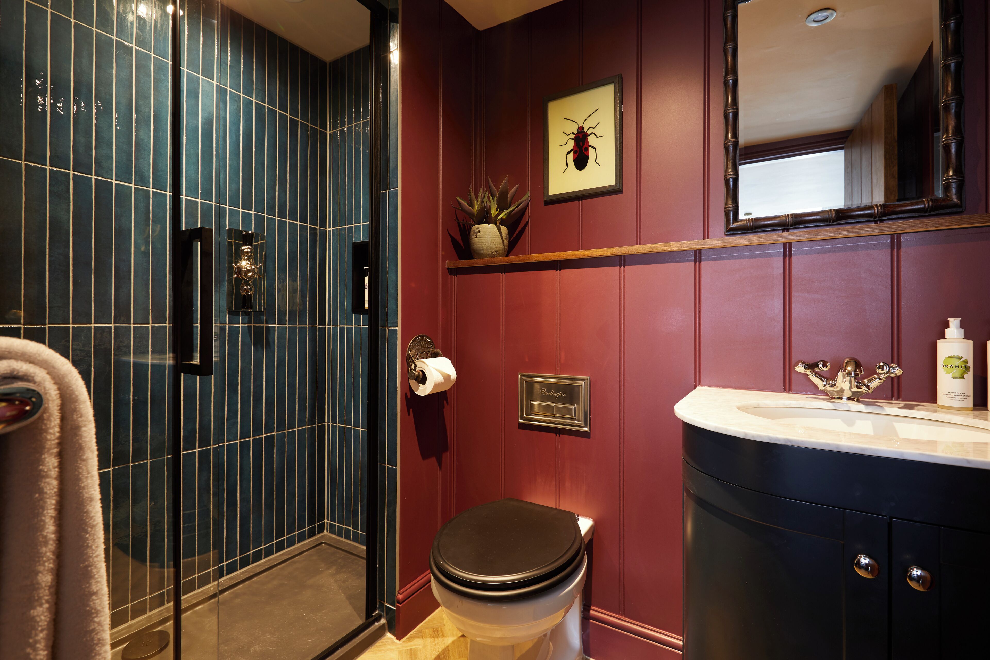 A bathroom with a glass shower enclosure, a toilet, a sink with a mirror above it, and a wall-mounted plant.
