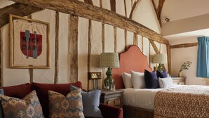 A room with a wooden ceiling, a bed with a patterned bedspread, a red sofa with patterned cushions, and a framed sign on the wall. - The Bull on Bell Street (Henley-on-Thames)