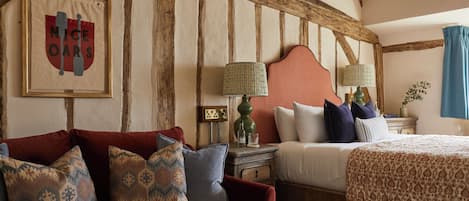 A room with a wooden ceiling, a bed with a patterned bedspread, a red sofa with patterned cushions, and a framed sign on the wall.