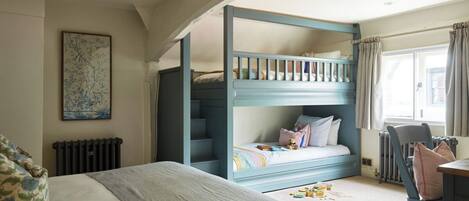 A bedroom with a bunk bed, a large bed, a radiator, a chair, and a window with curtains.