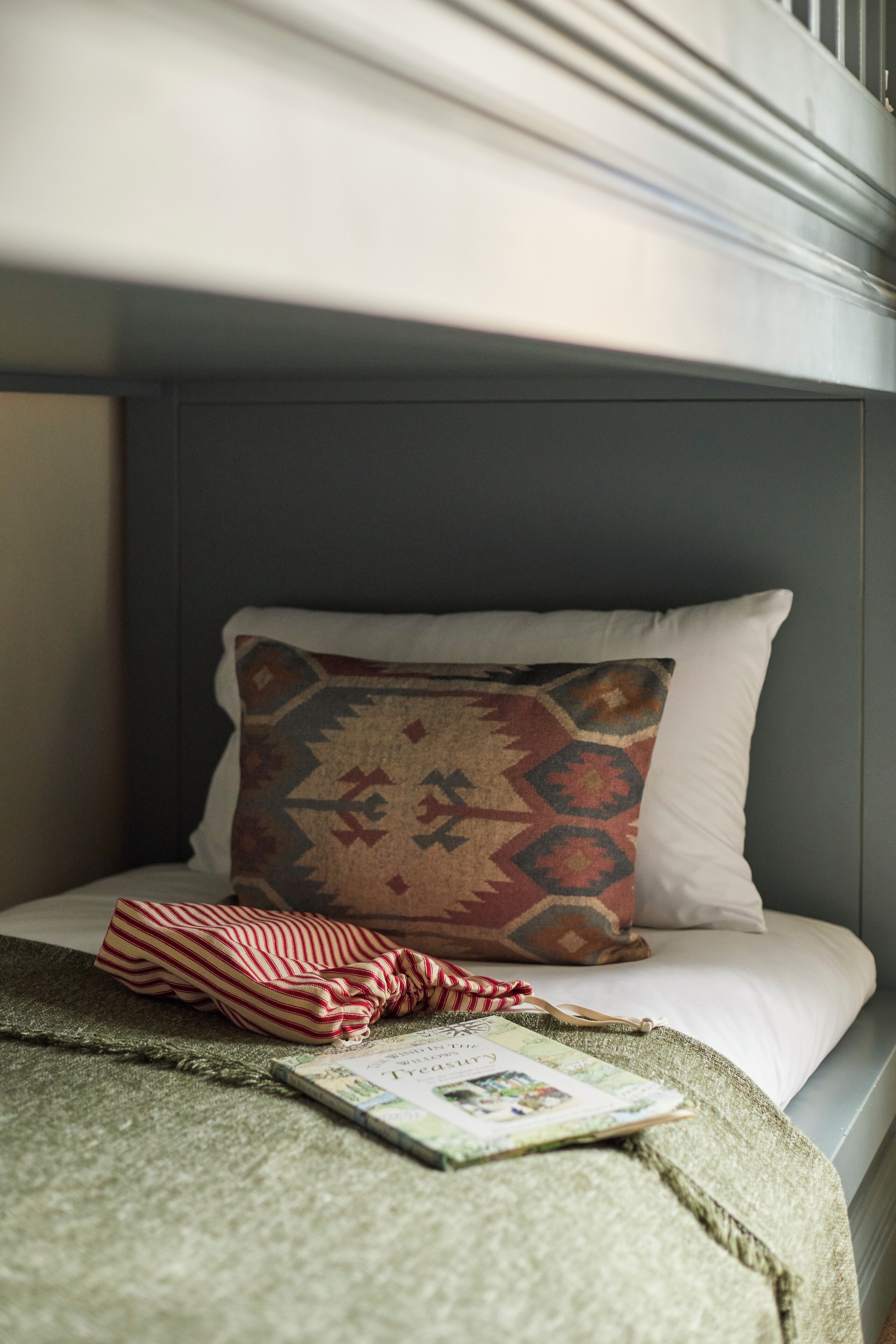 A bed with a patterned pillow, a striped blanket, and a book.