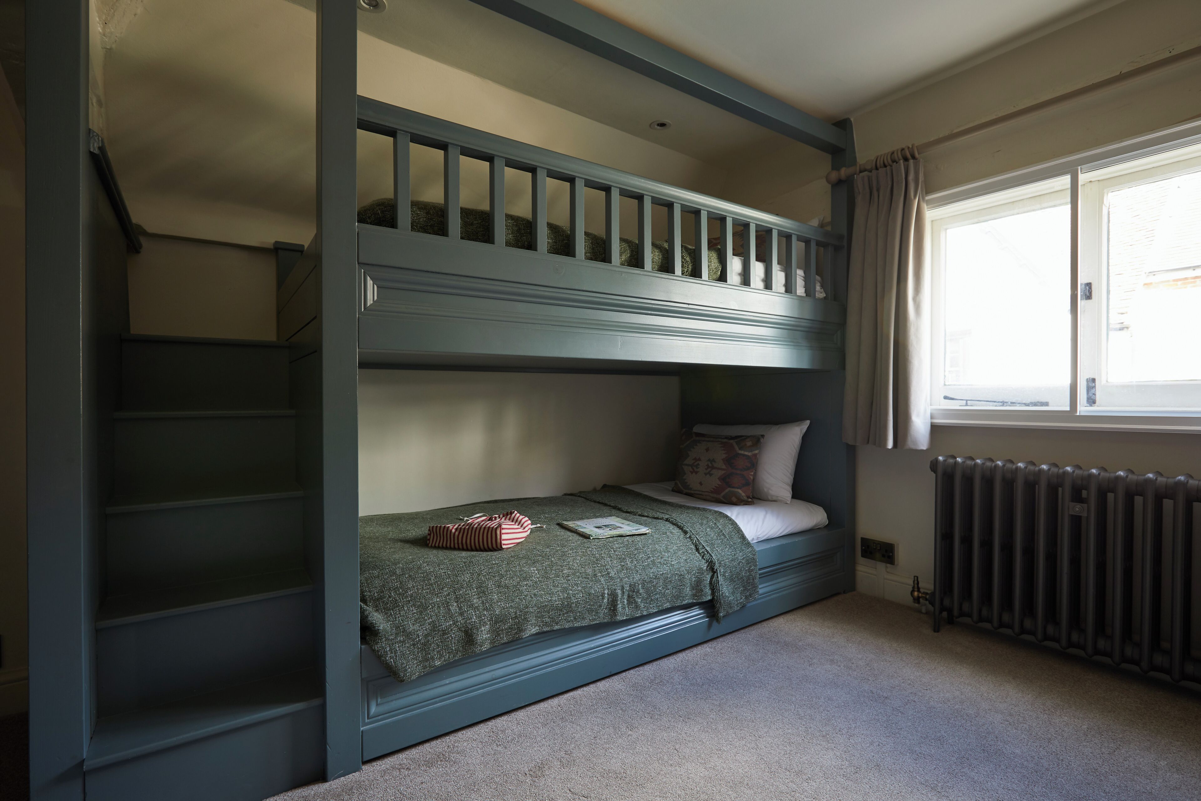 A bunk bed room with a window, a radiator, and a staircase.