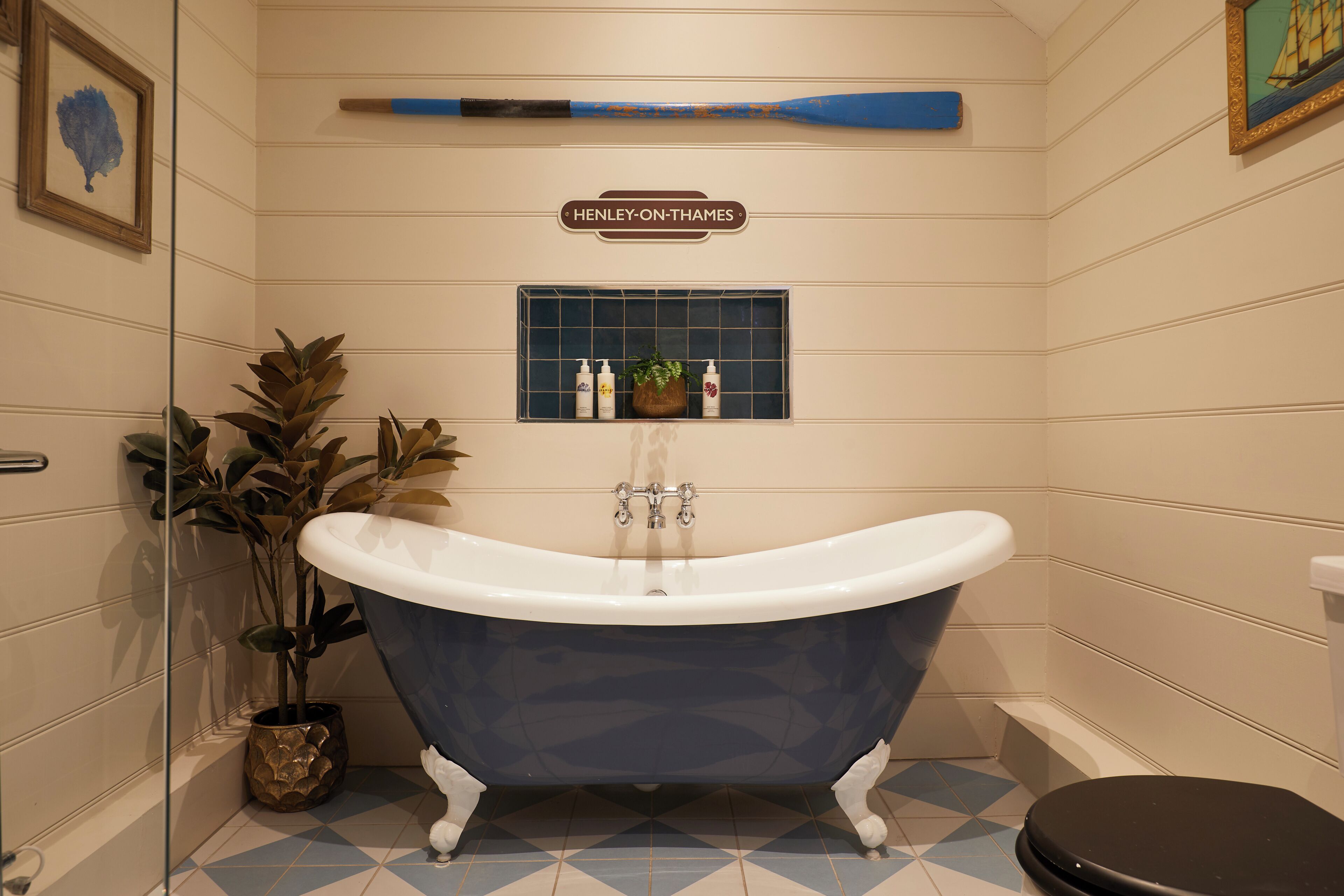 A bathroom with a clawfoot bathtub, a potted plant, a shelf with toiletries, and a sign above the bathtub.