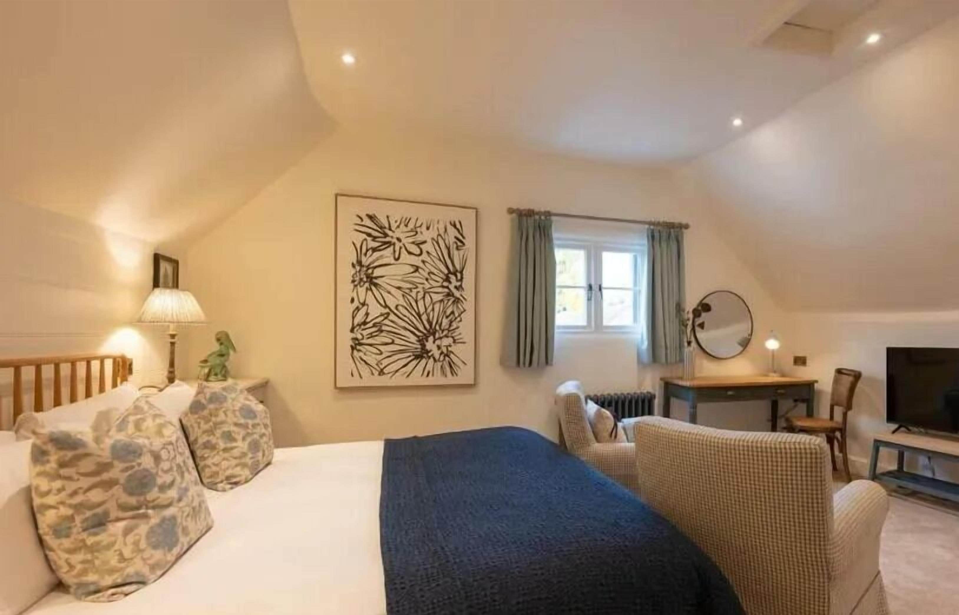 A bedroom with a bed, a desk, a chair, a TV, and a window with curtains.