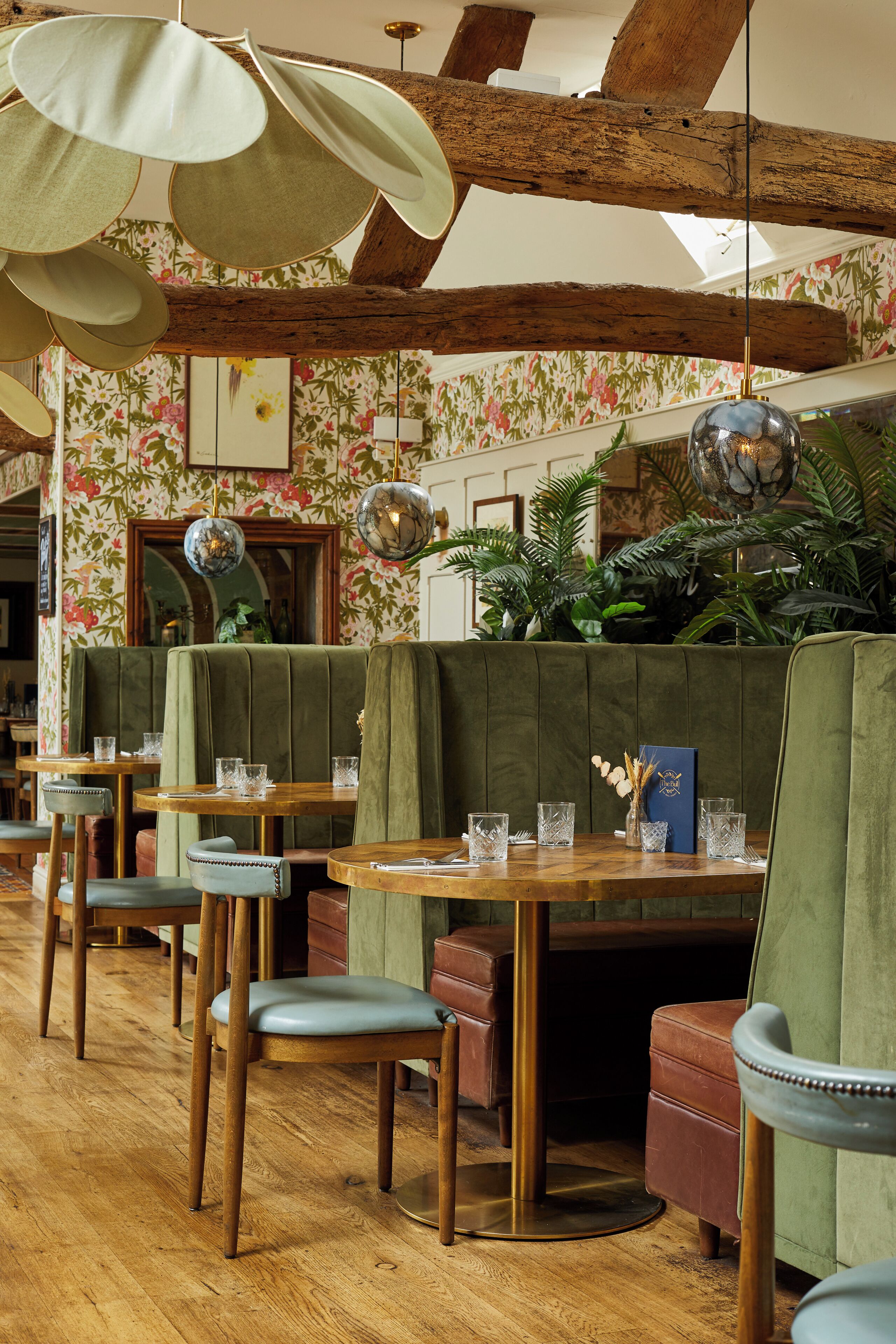 A restaurant interior with wooden tables, green upholstered booths, and hanging pendant lights.